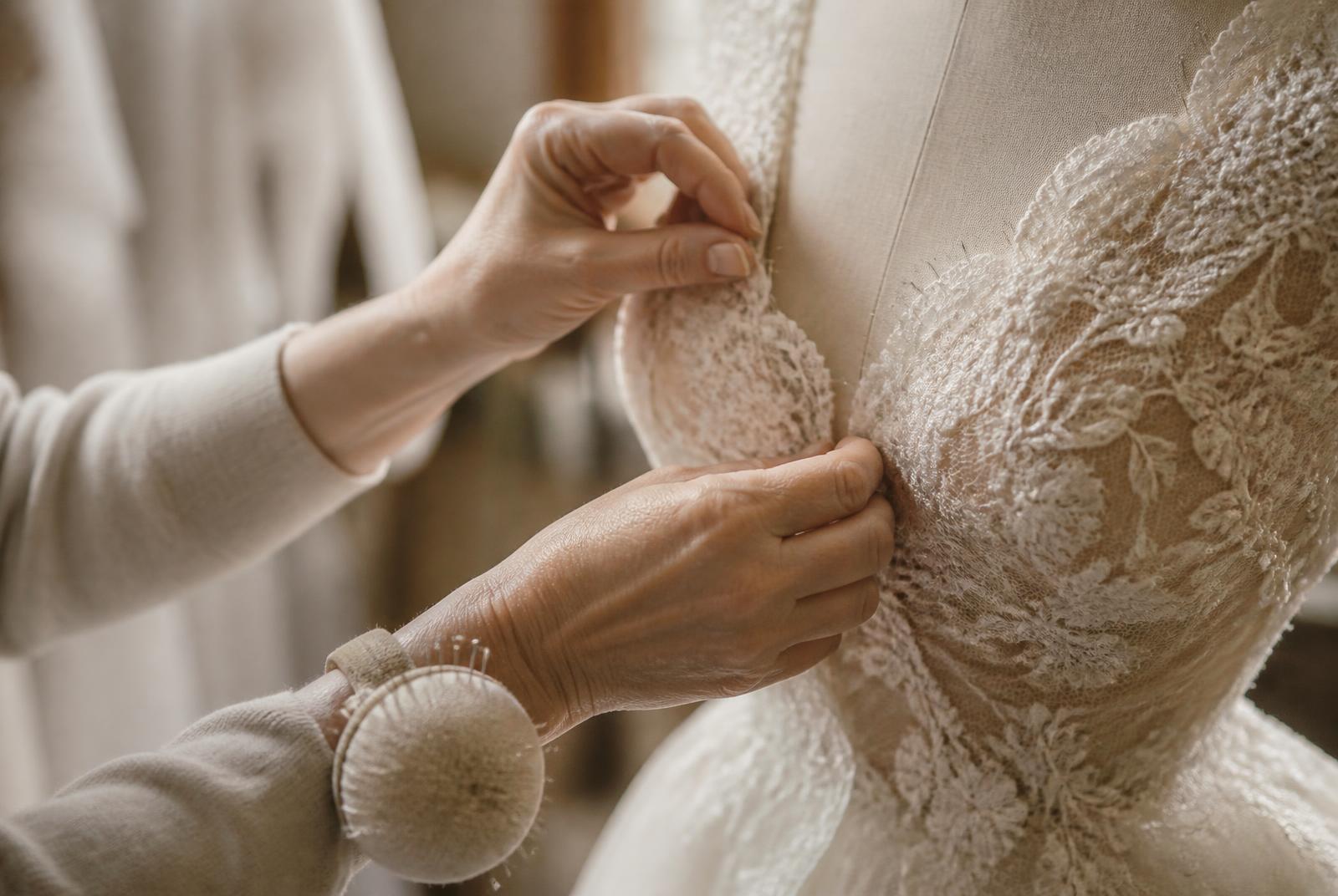 Alterations specialist pinning the lace bodice of an ivory wedding gown during a private bridal fitting